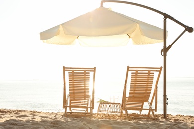 Wooden deck chairs, outdoor umbrella and table with cocktails on sandy beach. Summer vacation