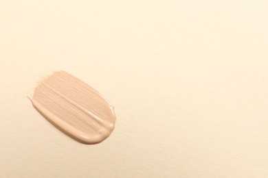 Photo of Smear of skin foundation on beige background, top view. Space for text