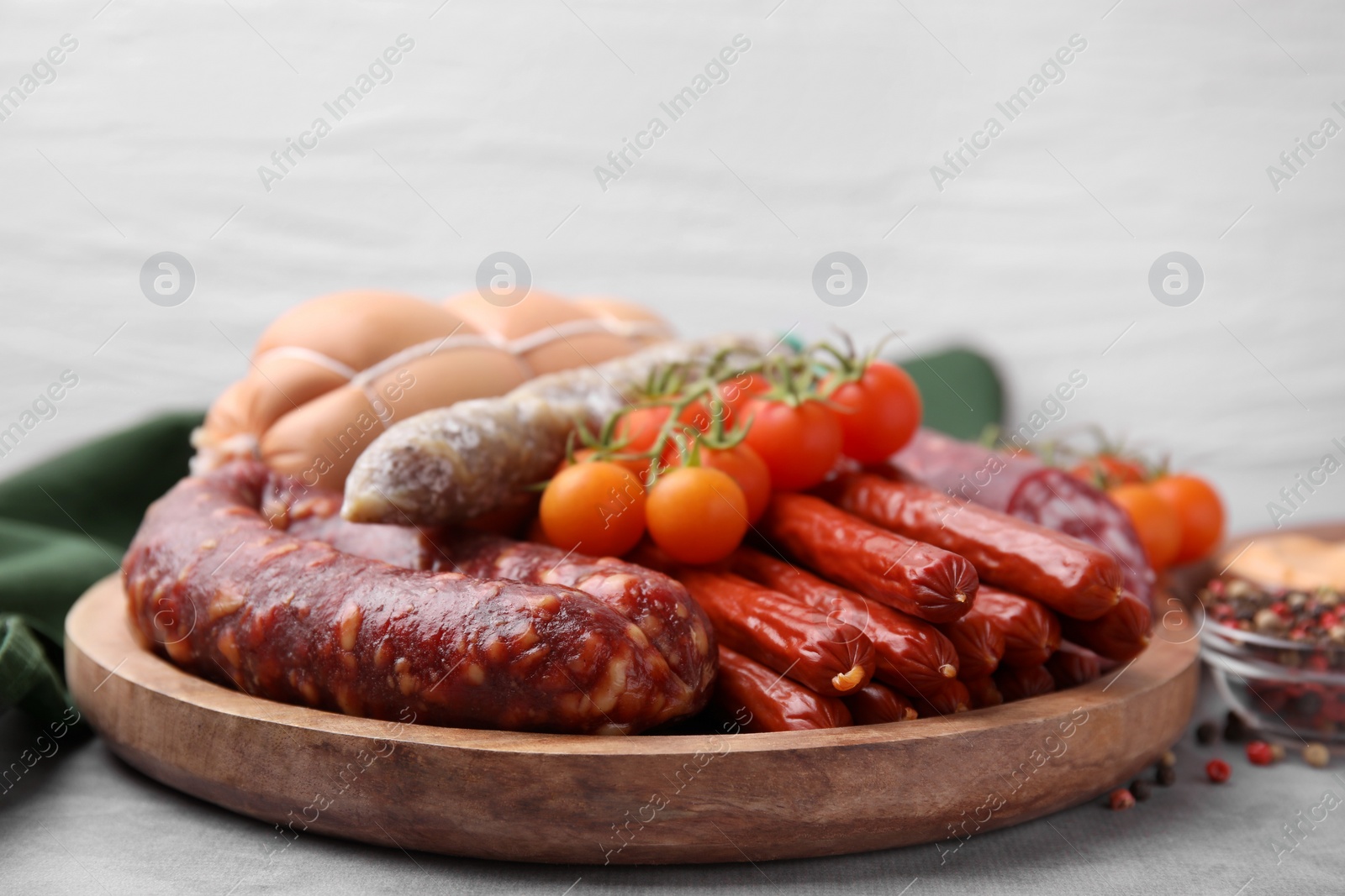 Photo of Different types of tasty sausages and tomatoes on light grey table, closeup