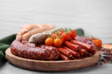 Different types of tasty sausages and tomatoes on light grey table, closeup