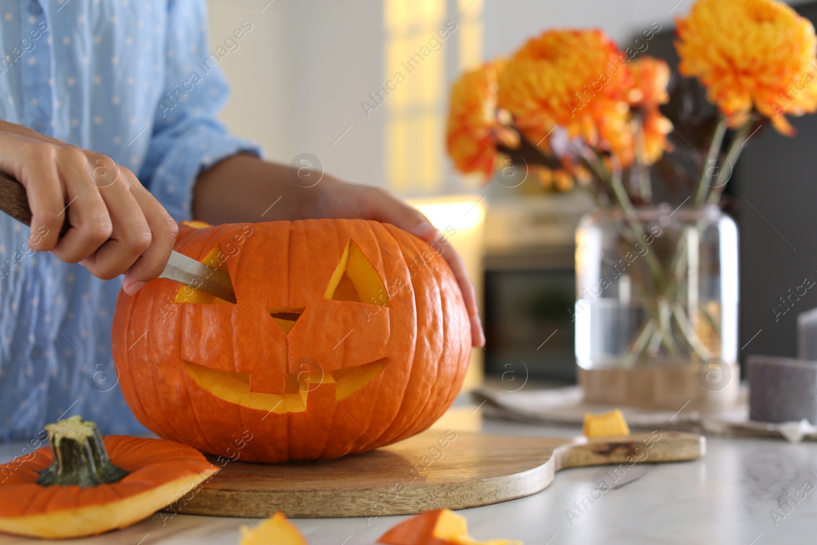 Photo of Woman making pumpkin jack o'lantern at table in kitchen, closeup. Halloween celebration