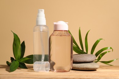 Photo of Bottlesmicellar water, green leaves and spa stones on wooden table against beige background