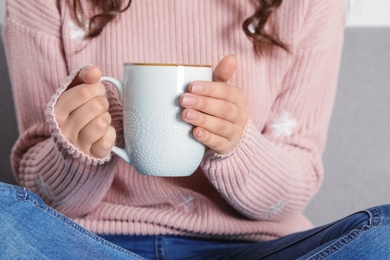 Photo of Young woman in warm sweater holding cup of hot drink, closeup