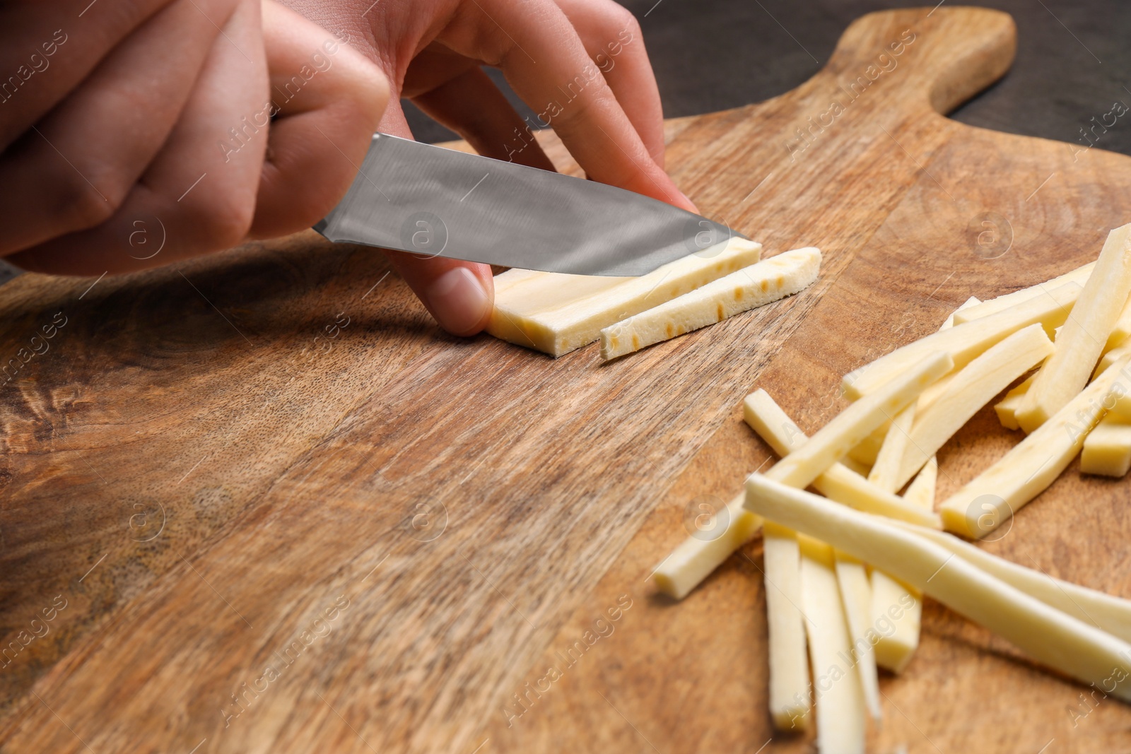 Photo of Woman cutting delicious fresh ripe parsnip at wooden board, closeup