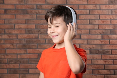 Photo of Cute little boy listening to music with headphones against brick wall
