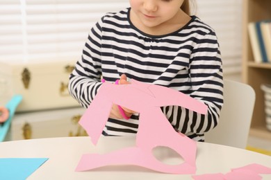 Photo of Girl cutting pink paper at desk in room, closeup. Home workplace