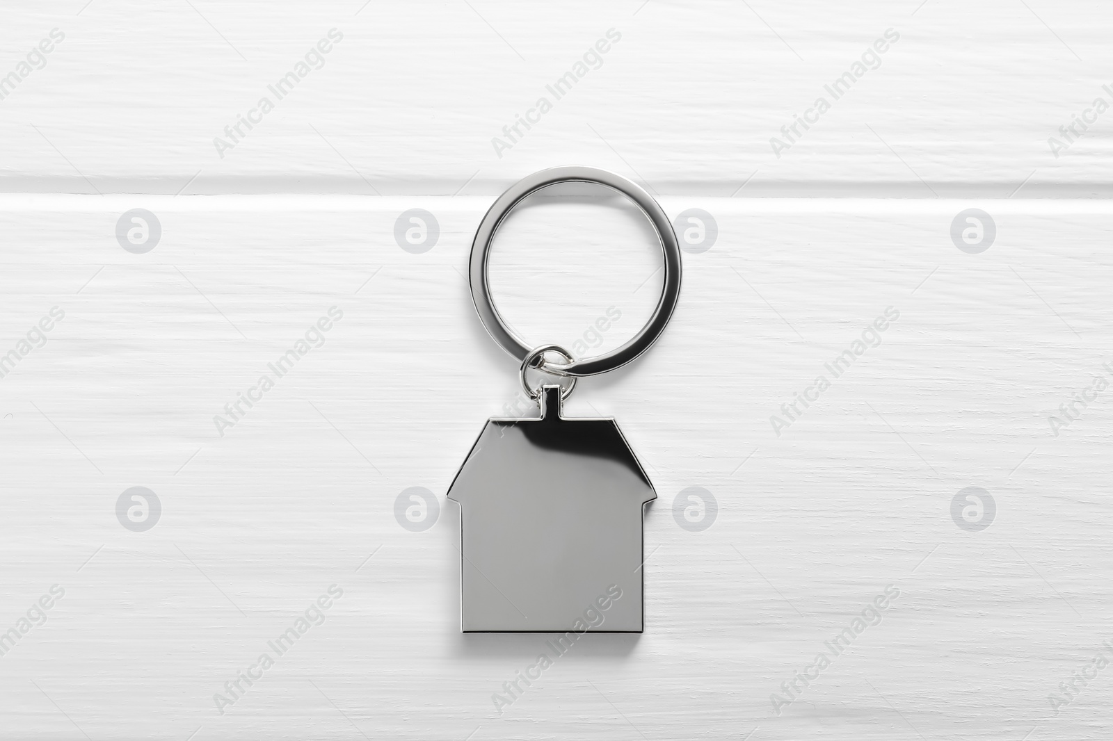 Photo of Metal keychain in shape of house on white wooden table, top view