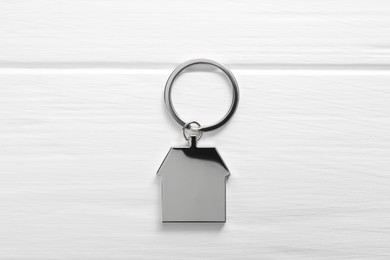 Metal keychain in shape of house on white wooden table, top view