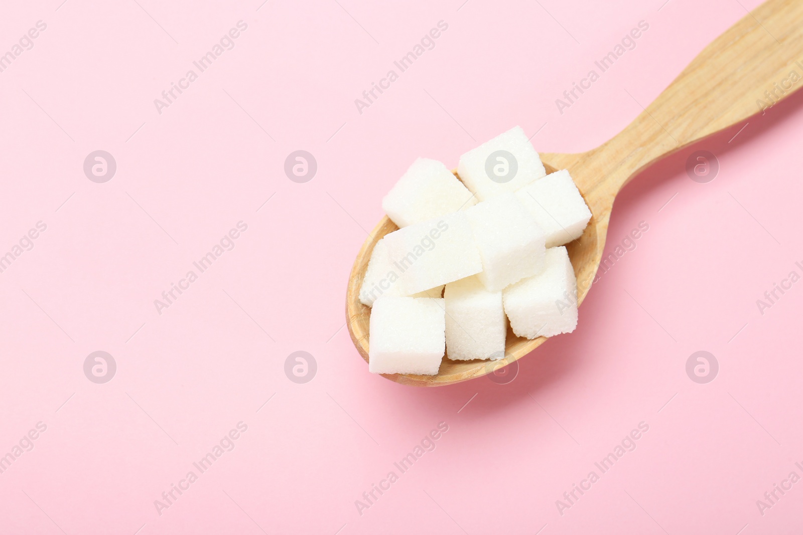 Photo of White sugar cubes in wooden spoon on pink background, top view. Space for text