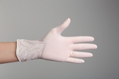 Person in medical gloves on grey background, closeup of hand