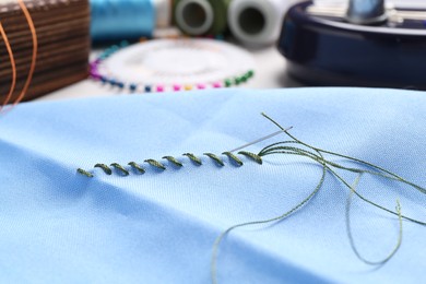 Photo of Light blue cloth with sewing needle, thread and stitches on table, closeup