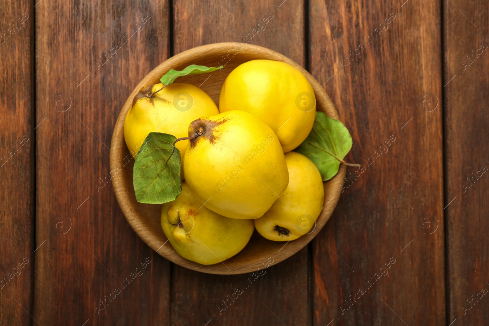 Photo of Tasty ripe quince fruits in bowl on wooden table, top view