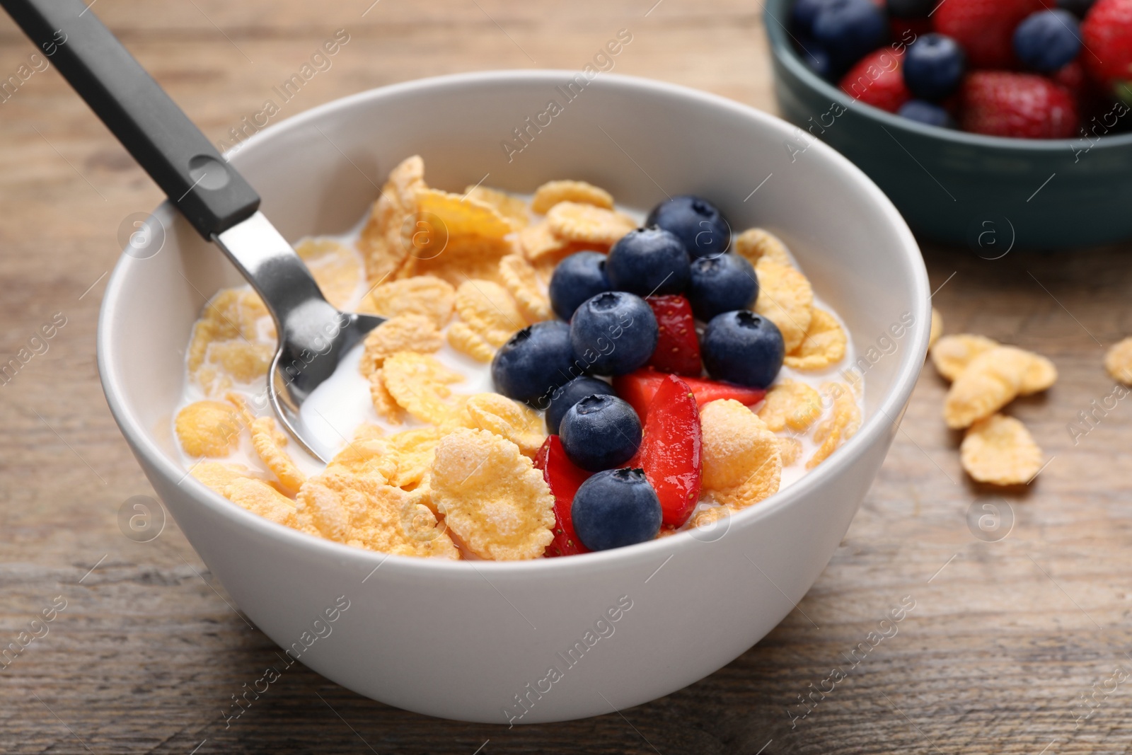 Photo of Bowl of tasty crispy corn flakes with milk and berries on wooden table, closeup