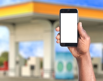 Image of African American man paying for refueling via smartphone at gas station, closeup. Device with empty screen