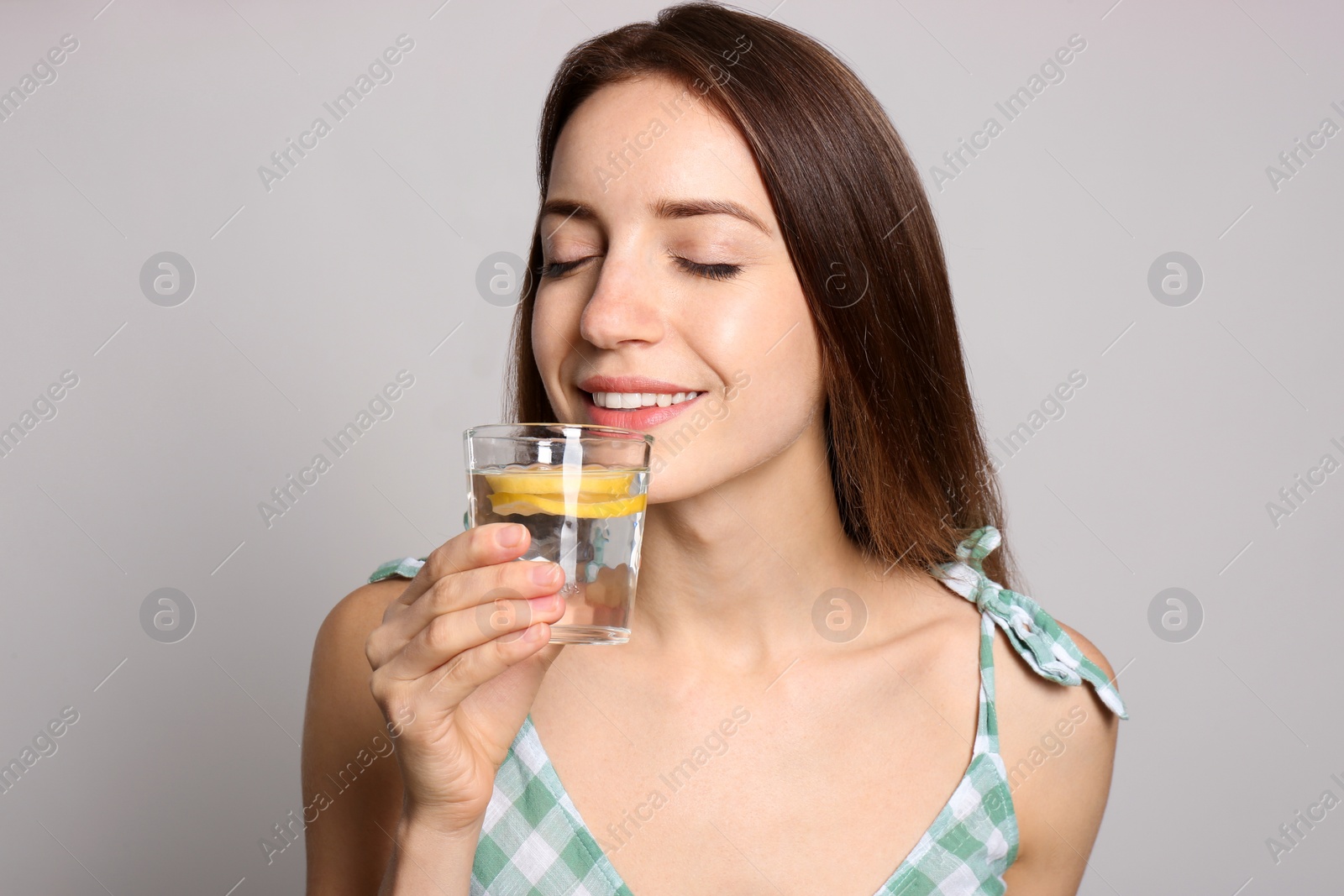 Photo of Young woman drinking lemon water on light background