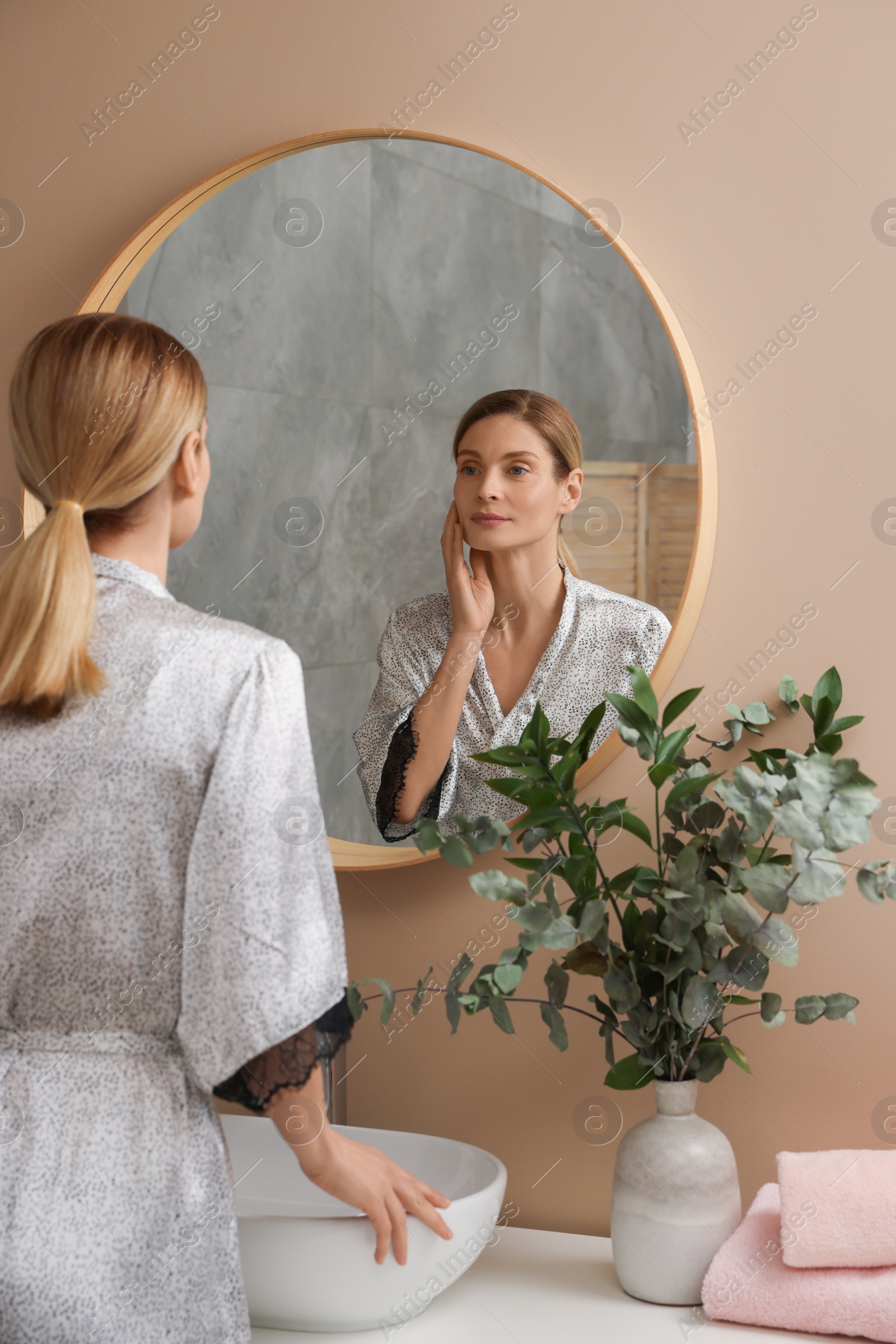 Photo of Woman massaging her face near mirror in bathroom