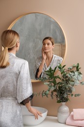 Woman massaging her face near mirror in bathroom