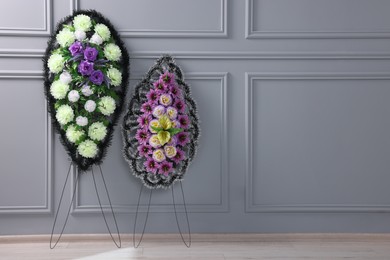 Photo of Funeral wreaths of plastic flowers near light grey wall indoors, space for text