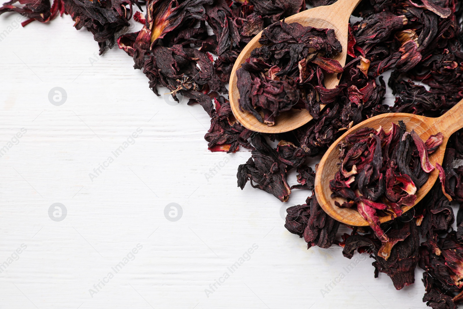 Photo of Spoons with dry hibiscus tea on white wooden table, flat lay. Space for text