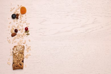 Photo of Tasty granola bar and ingredients on white wooden table, top view. Space for text