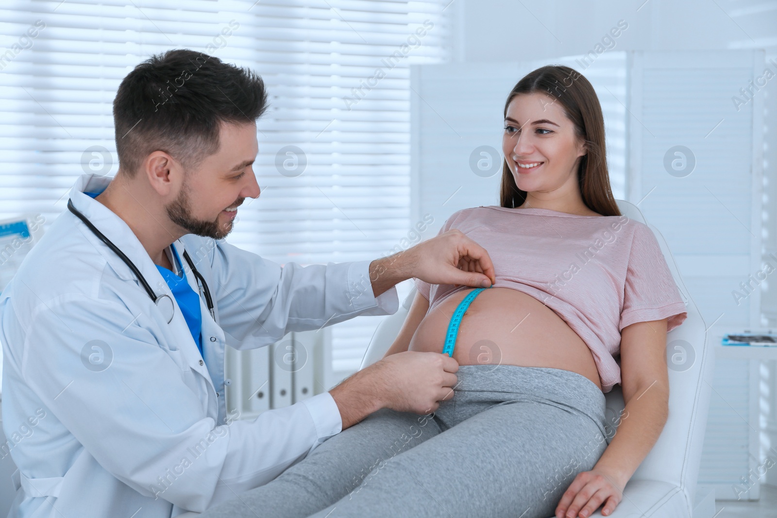 Photo of Doctor measuring pregnant woman's belly with tape in clinic