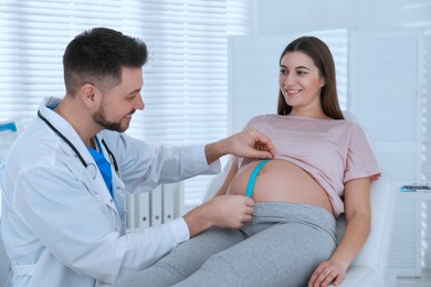 Doctor measuring pregnant woman's belly with tape in clinic