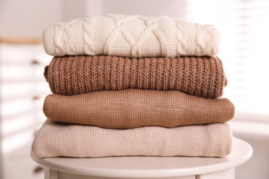 Stack of folded warm sweaters on white table indoors, closeup