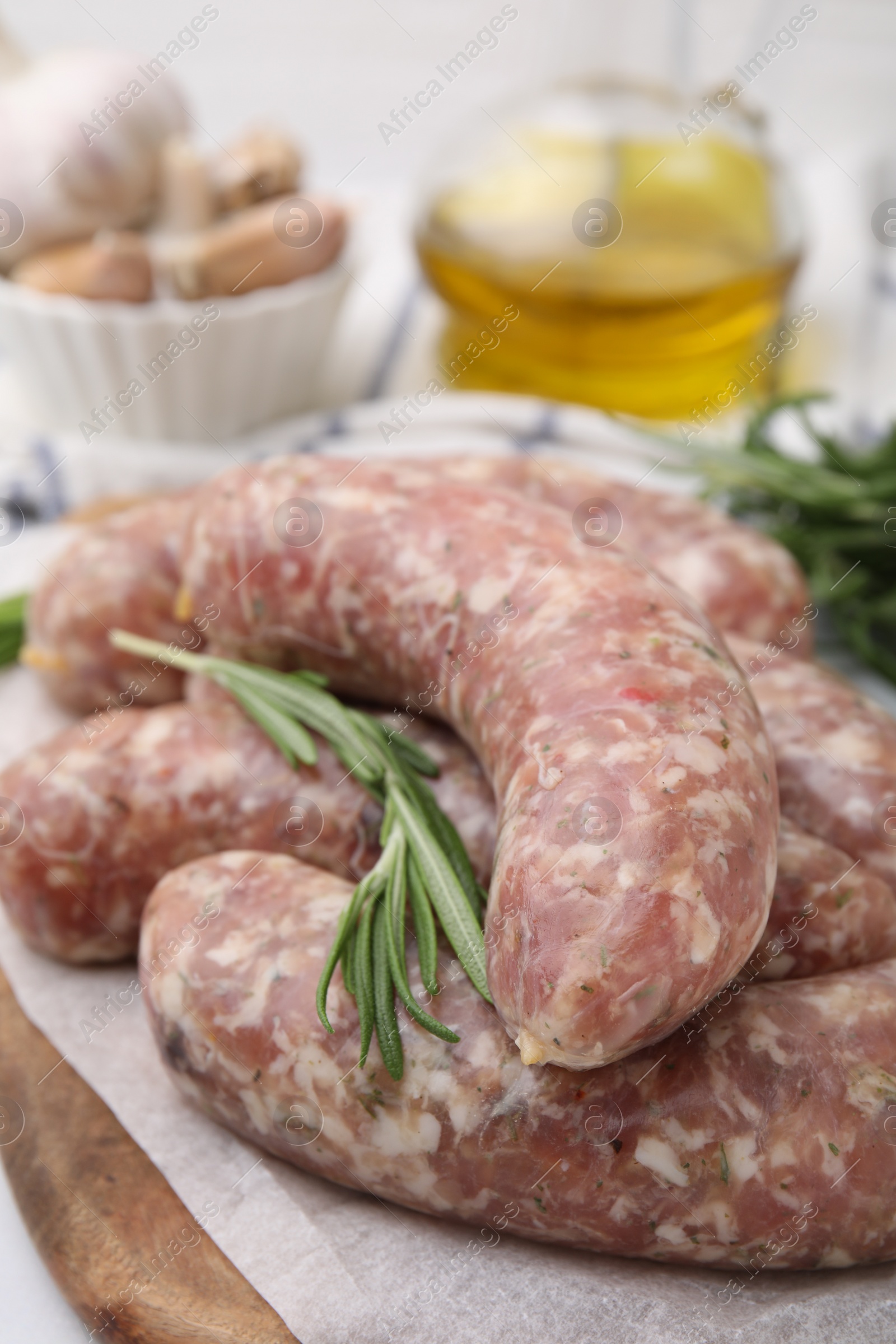 Photo of Raw homemade sausages and rosemary on white table, closeup