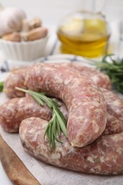 Raw homemade sausages and rosemary on white table, closeup