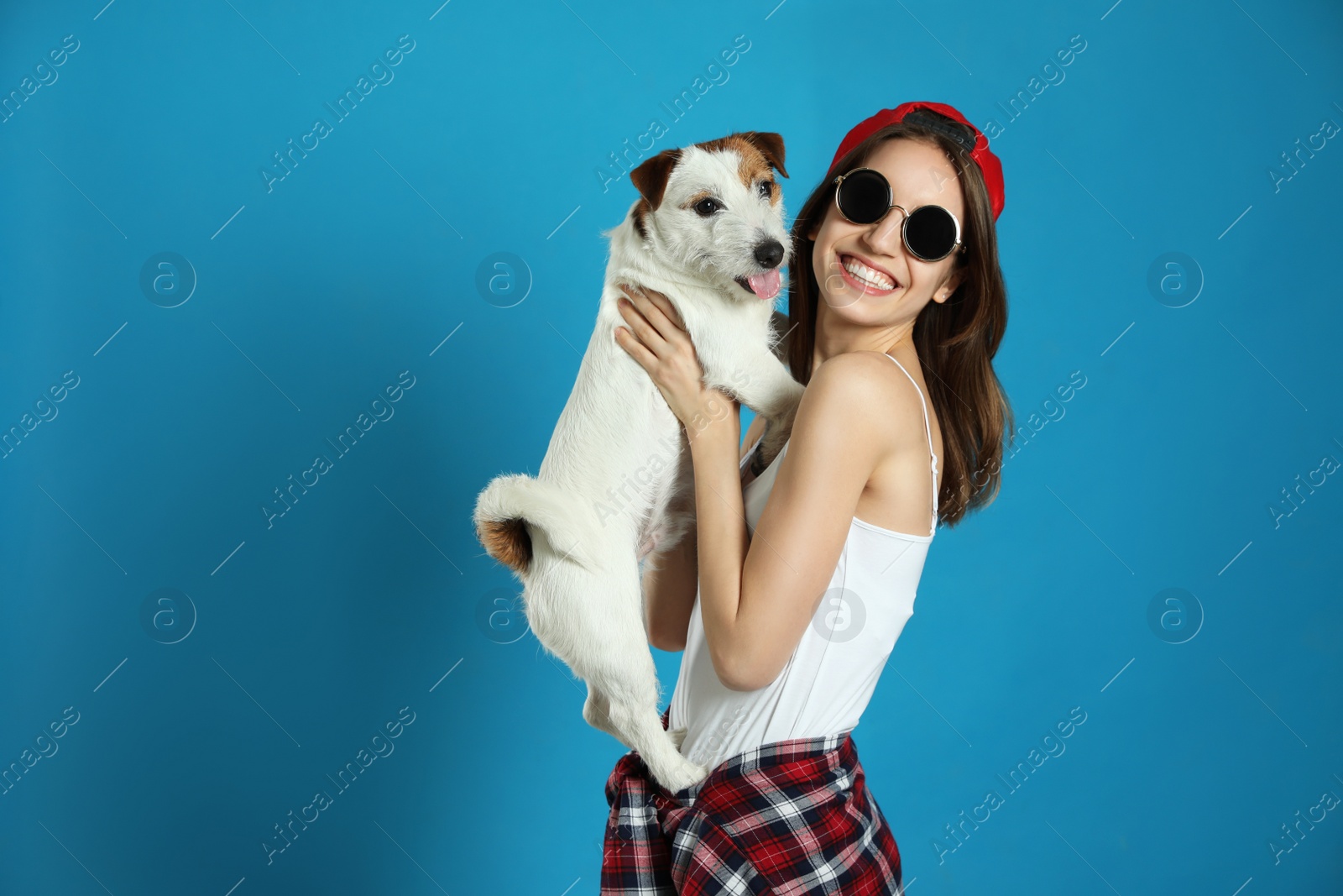 Photo of Young woman with her cute Jack Russell Terrier on light blue background. Lovely pet