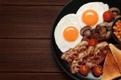 Photo of Plate of fried eggs, mushrooms, beans, bacon, tomatoes and toasted bread on wooden table, top view with space for text. Traditional English breakfast
