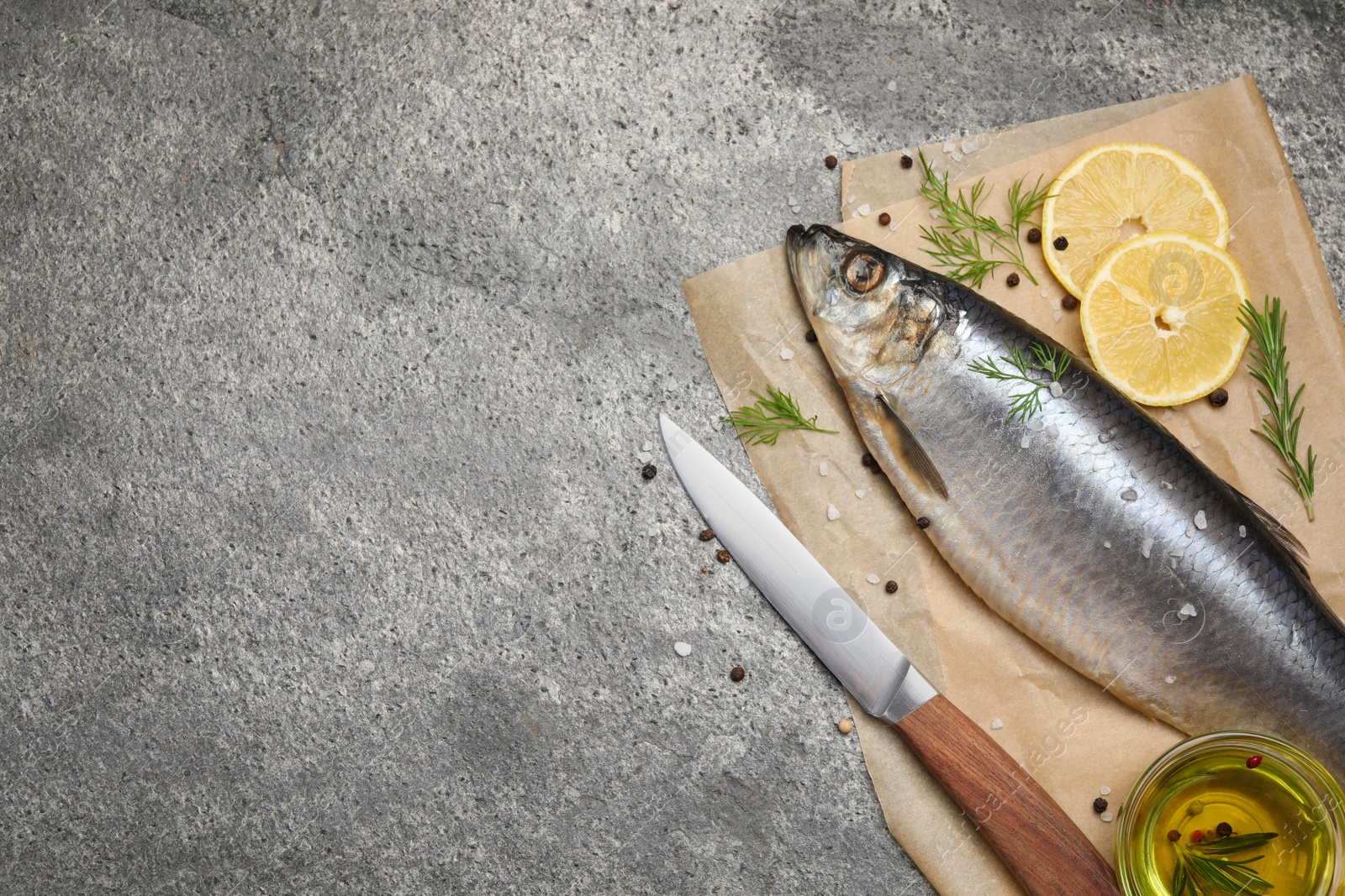 Photo of Delicious salted herring, olive oil, lemon and rosemary on grey table, top view. Space for text