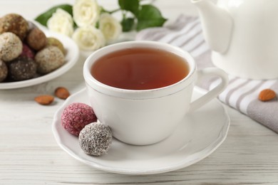 Photo of Cup of aromatic tea and delicious vegan candy balls on white wooden table