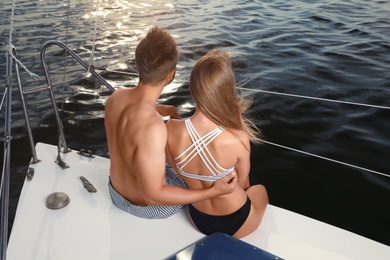 Young man and his beautiful girlfriend in bikini sitting on yacht. Happy couple on vacation
