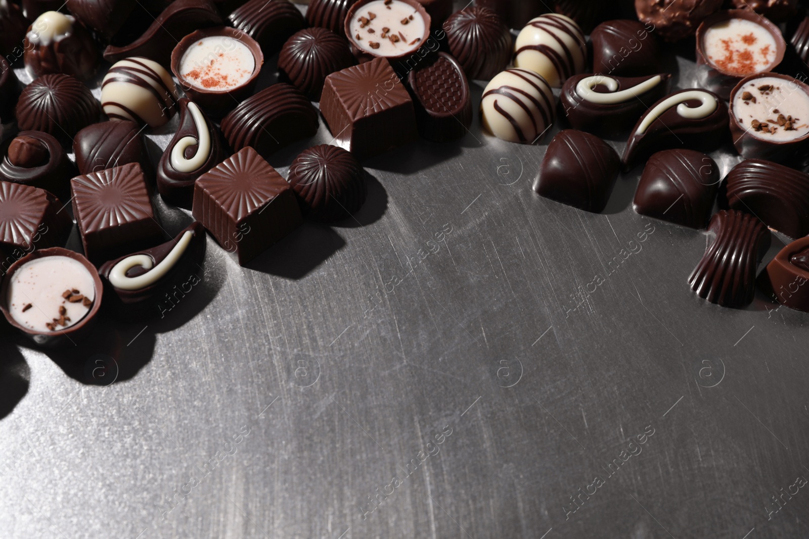 Photo of Many different delicious chocolate candies on metal surface. Space for text