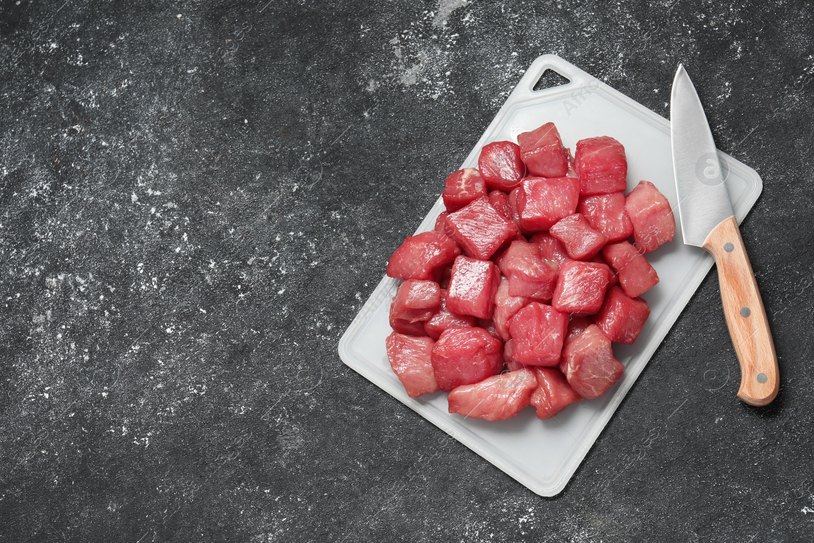 Photo of Cooking delicious goulash. Raw beef meat and knife on grey textured table, top view. Space for text