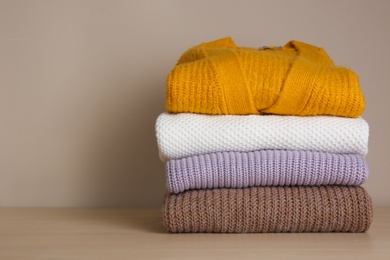 Photo of Stack of folded knitted sweaters on wooden table. Space for text