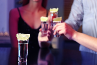 Photo of Mexican Tequila shot on table and young people toasting in bar