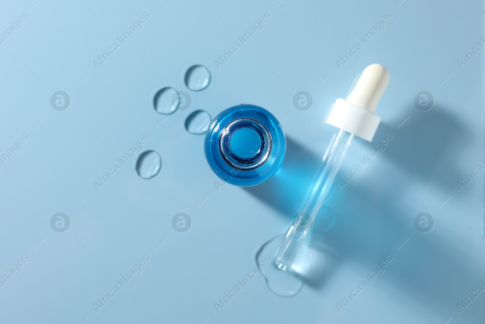 Photo of Open bottle of cosmetic serum on light blue background, top view