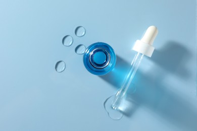 Photo of Open bottle of cosmetic serum on light blue background, top view