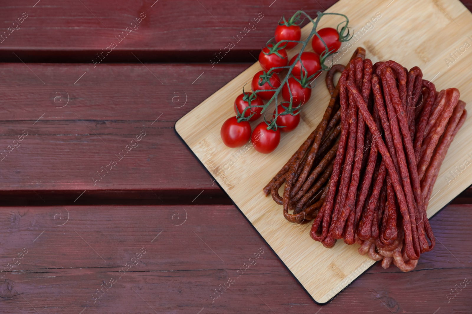 Photo of Tasty dry cured sausages (kabanosy) and tomatoes on wooden table, flat lay. Space for text