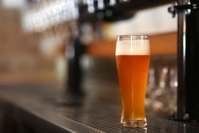 Photo of Glass of cold tasty beer on bar counter, space for text