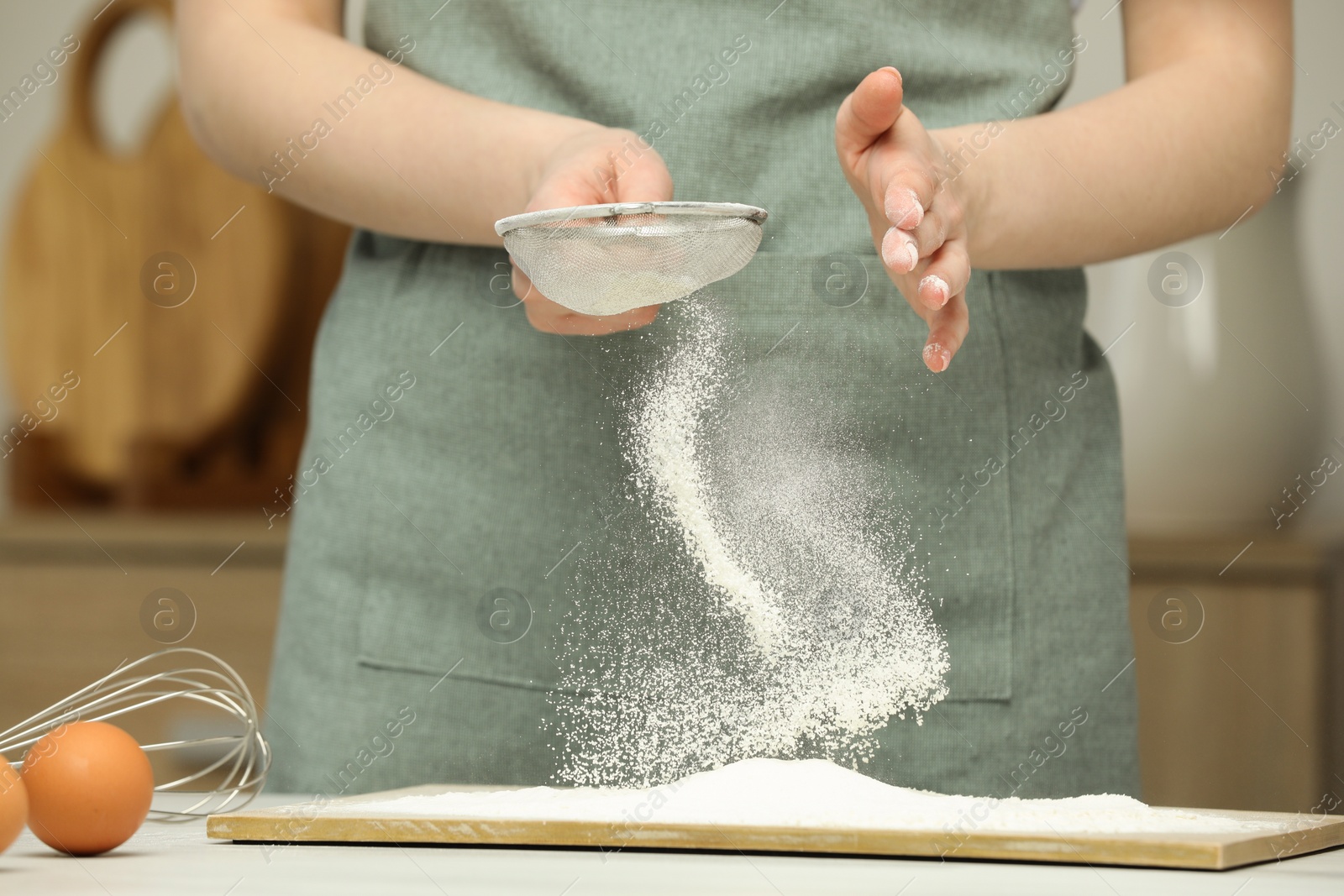 Photo of Woman sieving flour at table in kitchen, closeup