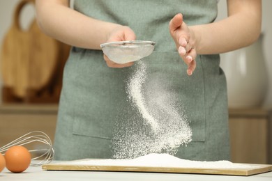 Photo of Woman sieving flour at table in kitchen, closeup