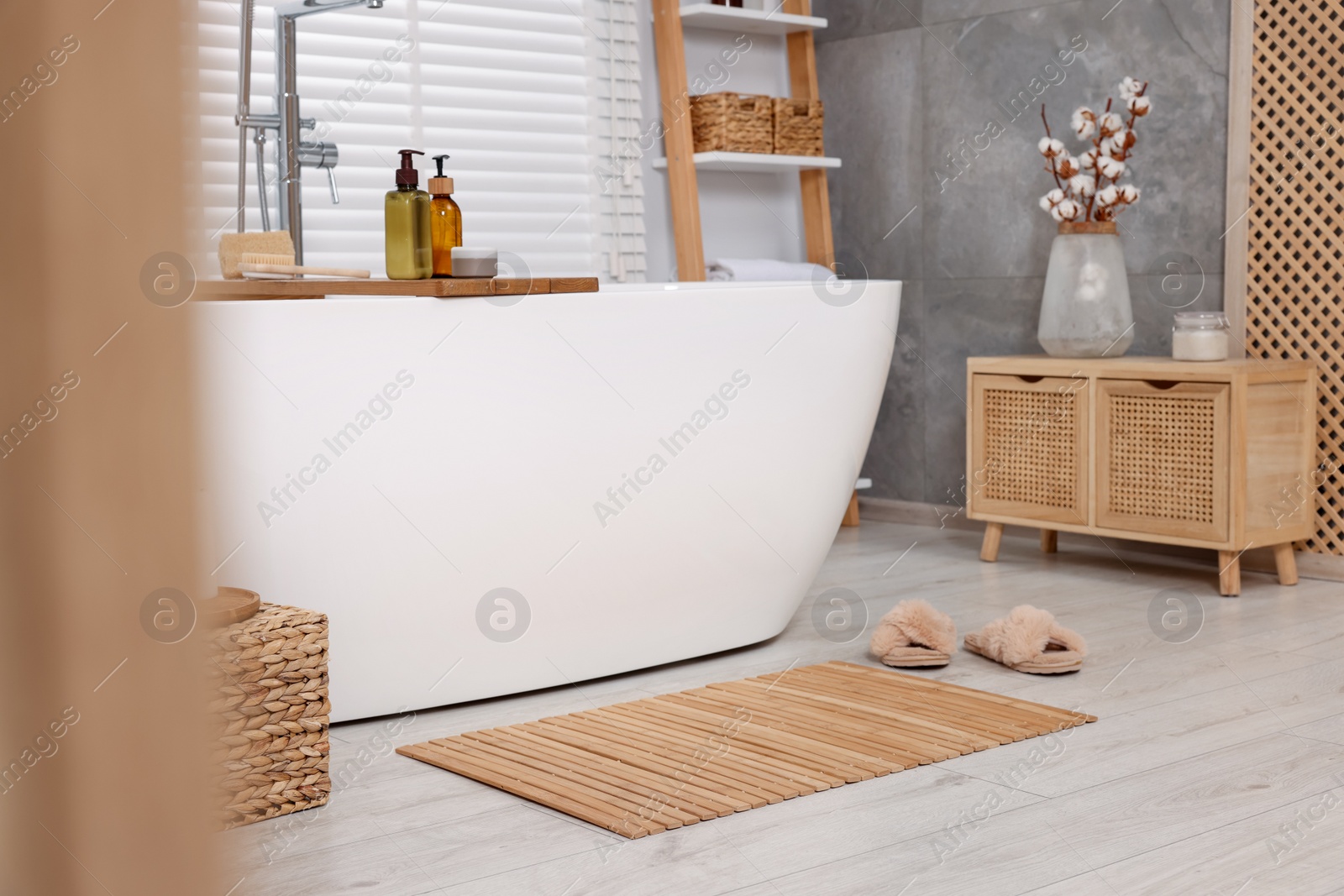 Photo of Stylish bathroom interior with bamboo bath mat and white tub