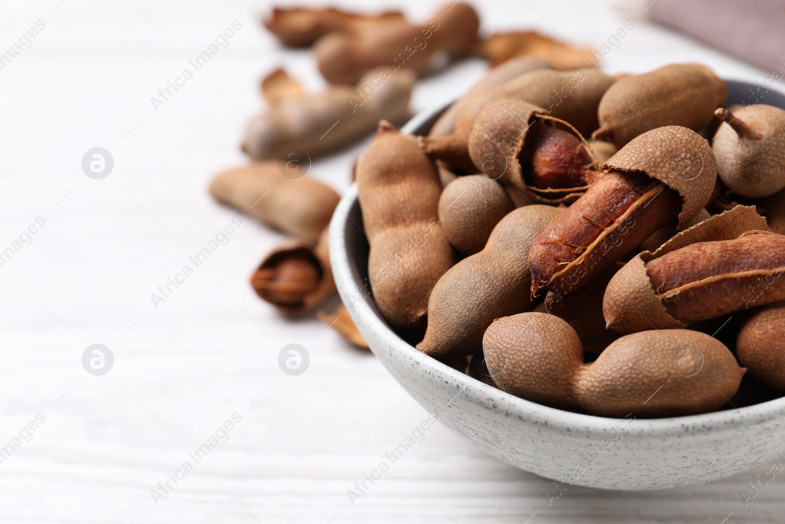 Photo of Delicious ripe tamarinds in ceramic bowl on white wooden table, closeup. Space for text