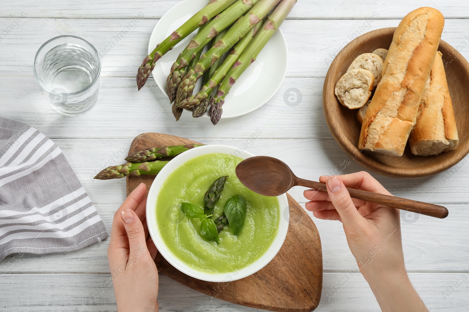 Photo of Woman eating delicious asparagus soup at white wooden table, top view