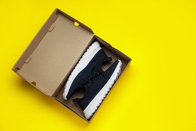Photo of Comfortable sports shoes in cardboard box on yellow background, top view. Space for text