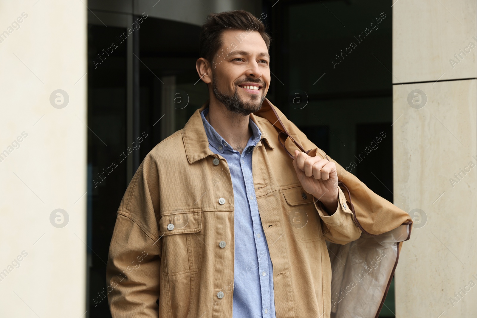 Photo of Attractive happy man holding garment cover with clothes outdoors. Dry cleaning service