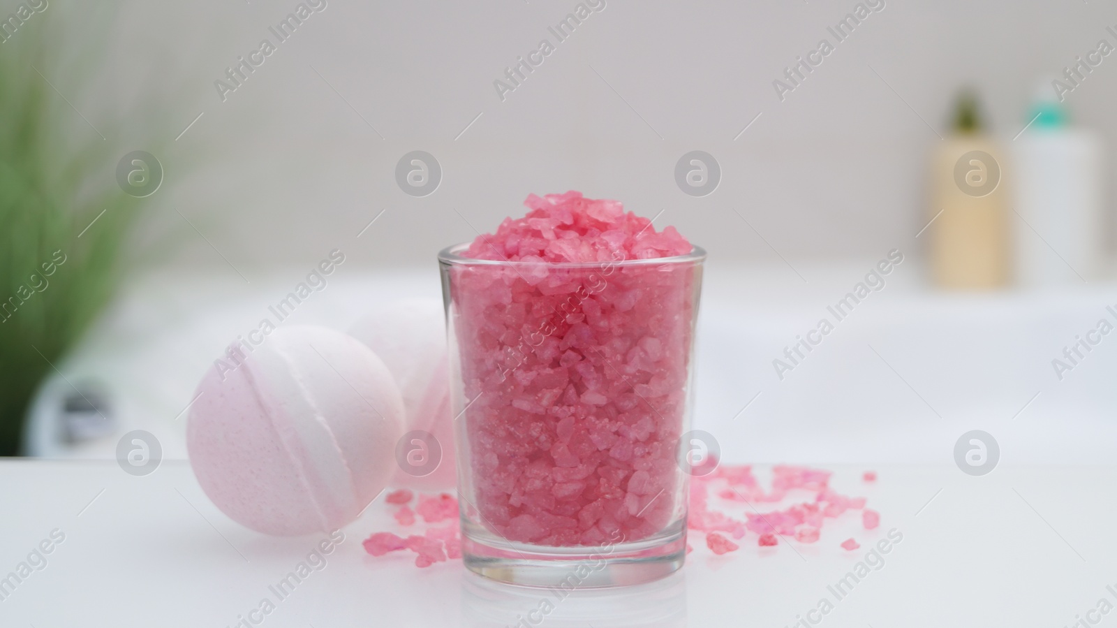 Photo of Glass with sea salt and bath bombs on table in bathroom, closeup